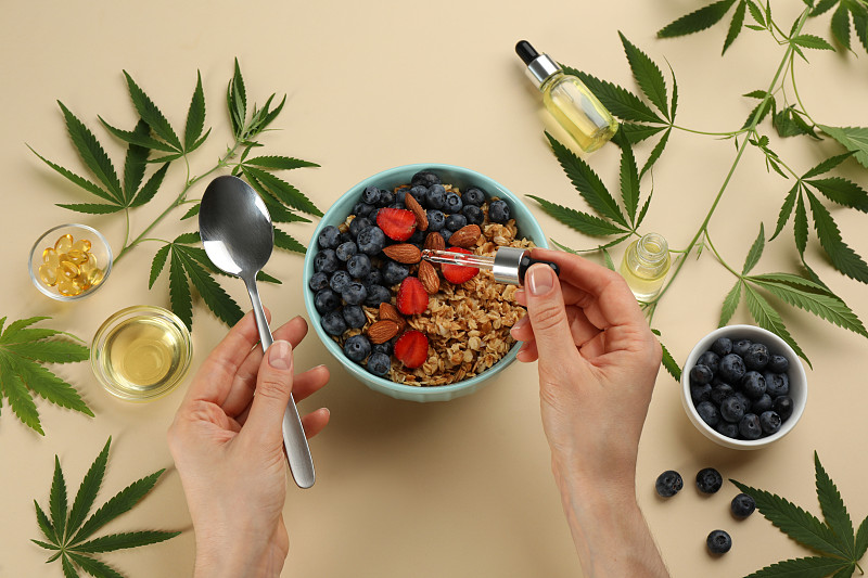 俯视图的女人滴THC酊剂或CBD油到燕麦碗米色背景，特写