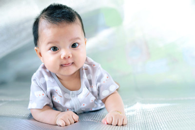 东南亚的新生婴儿正在地板上爬行。新生儿穿着灰色衬衫。宝宝是东南亚人。孩子是可爱的。孩子在室内拍照。婴