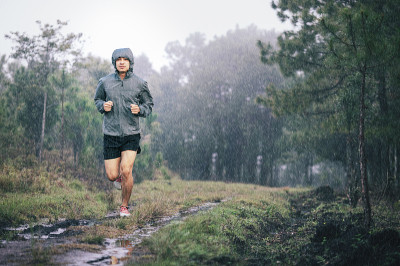 运动员跑步在灰色运动夹克森林小径在雨中