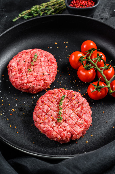 生的碎牛肉汉堡牛排在平底锅里的肉片。黑色背景。俯视图
