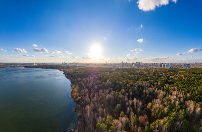 日落湖岸的秋天森林，地平线上的城市，鸟瞰图