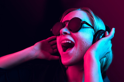 时尚漂亮的女人戴着耳机听音乐的霓虹灯背景