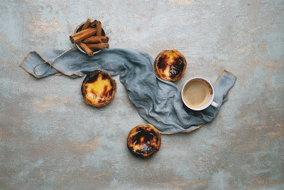 柔和的de nata。传统的葡萄牙甜点，鸡蛋挞在乡村背景下，肉桂棒在过滤器和咖啡杯装饰餐巾。俯视图
