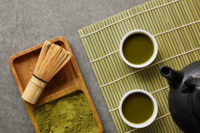 俯视图的绿色抹茶粉与竹搅拌器在木板茶壶和白色杯与绿茶在桌子垫
