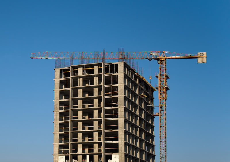 在蓝天下的建筑工地上，塔吊正在建造一座新的住宅楼。建筑行业的改造方案、发展、理念。