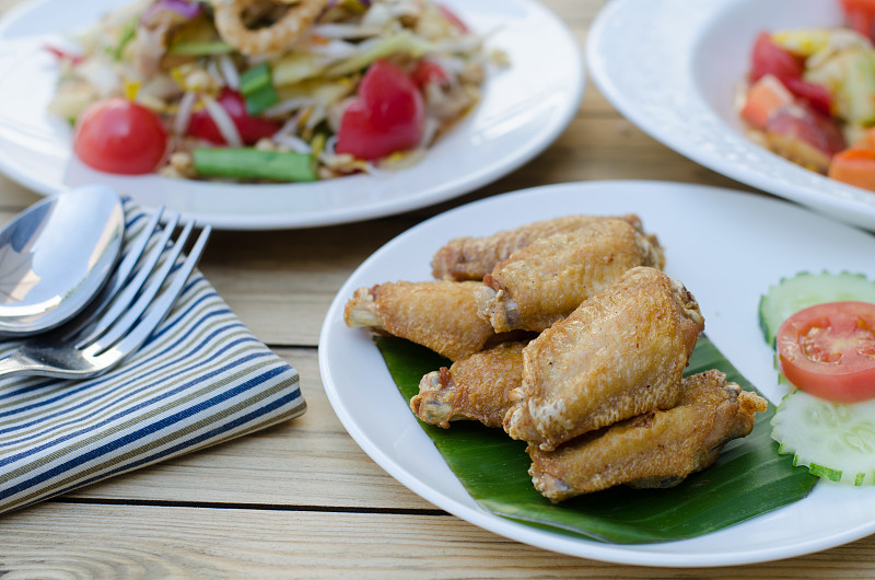 泰国的饮食文化。白盘炸鸡和木桌木瓜沙拉，选择焦点