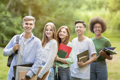 大学的朋友。户外肖像的多元种族学生与工作簿一起摆姿势