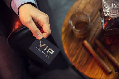 男子持有VIP会员卡。从上往下看，先生的手拿着独家VIP会员卡旁边的木桌上有威士忌和雪茄。