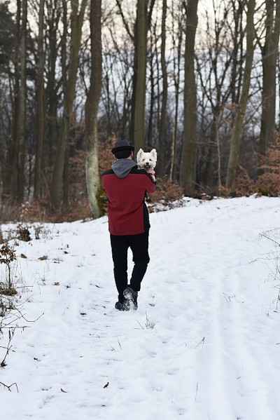 一个男人抱着一只白色的狗，走在雪景中