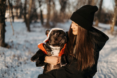 美丽的十几岁的女孩抱着一只法国斗牛犬在她的手臂在冬天。公园里遛狗的女孩