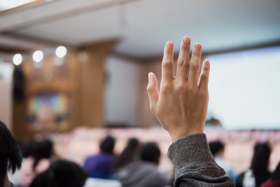 听众或学生在会议上举手回答问题，而演讲者在研讨会大厅与人群演讲，教室里的大群手臂进行投票或提问