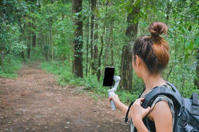 年轻女性使用智能手机和万向节当她在森林中徒步旅行时，灵感、动机和露营活动的概念