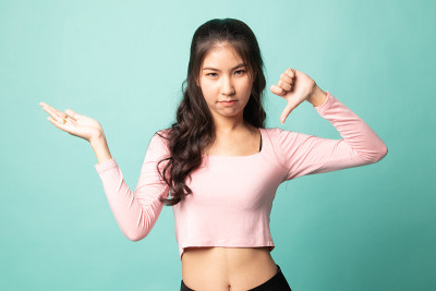 年轻的亚洲妇女显示手掌和拇指向下。