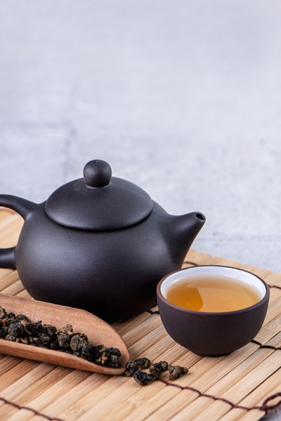黑色茶壶和茶杯中的热茶和干茶叶在明亮的灰色水泥背景。