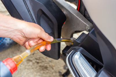 修理和保养摩托车。换油。汽车修理工通过一根橡胶软管把油注入发动机