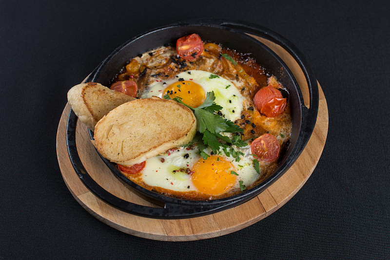 健康早餐shakshuka——鸡蛋，洋葱，甜椒，西红柿和香料放在铸铁炖锅里，放在旧木板上。