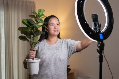 亚洲女性用智能手机在线直播，在家里卖人造植物