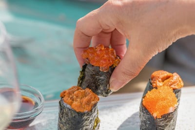 一个男人的手把一块寿司放在放在桌子上的一种食物切菜板上。