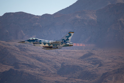 F-16“战斗猎鹰”以侵略者的颜色对抗内华达山脉，导弹在机翼上，加力燃烧器和飞机后面可见的喷射流