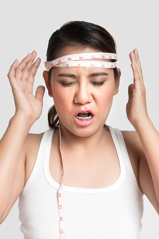 一个亚洲女人在量他的头，因为节食而疯了