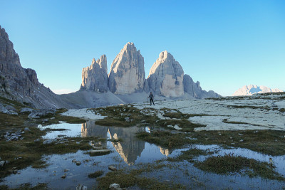 一名男子徒步旅行，欣赏意大利Dolomites地区的Drei Zinnen山。群山倒映在小桨里。荒凉