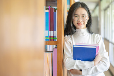 回到学校教育知识学院的大学理念，美丽的女大学生抱着她的书微笑着站在图书馆，学习和教育的理念
