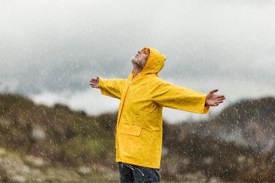 旅人穿着黄色雨衣在云山中风雨交加