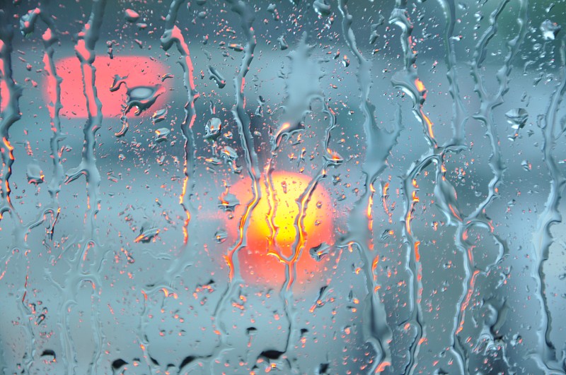 模糊的雨滴在汽车窗户与道路光散焦在雨季抽象的背景。水滴纹理玻璃上的雨在汽车驾驶的概念