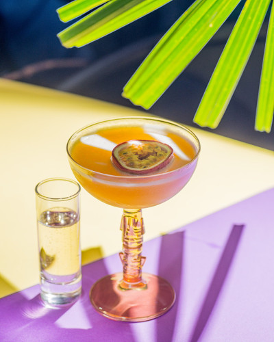黄色的热带鸡尾酒配上百香果，以热带植物的叶子和遮阳伞为背景拍摄。颜色背景