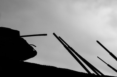 一辆坦克的剪影映衬着乌云密布的天空和反坦克的刺刀武器，象征着战争和冲突