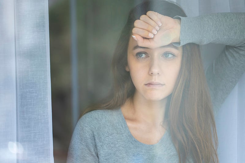 沉思的年轻女子透过窗户看