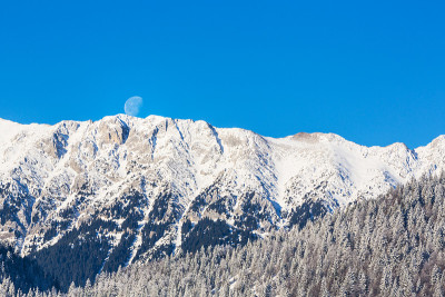 冬天的风景在山上，有白雪覆盖的山峰和落日的月亮
