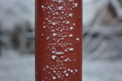 冬天下雪时，红色的金属管上覆盖着大而蓬松的雪花。
