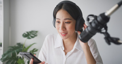 一名年轻的亚洲女性在家庭录音室用笔记本电脑录制播客。