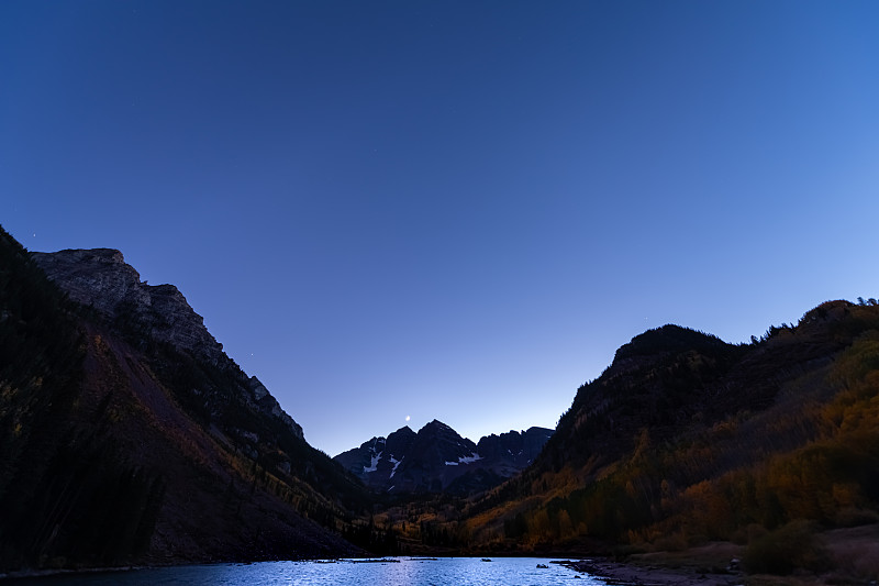 2019年10月，在科罗拉多州的阿斯彭，栗色的钟湖宽角度观看夜晚的夜空和岩石山峰，水中的月亮倒影