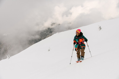 男子滑雪者用登山杖在雪山小道上，背景是多云的天空。