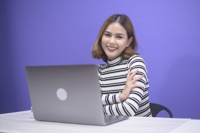 年轻漂亮的女人正在用她的电脑在蓝色背景上工作。