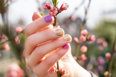 女性手用金色和紫色指甲设计握着花枝。