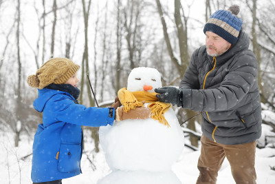 小男孩和他的父亲在下雪的公园堆雪人。爸爸和儿子为雪人系了一条围巾。冬季与孩子们一起活跃户外休闲活动。