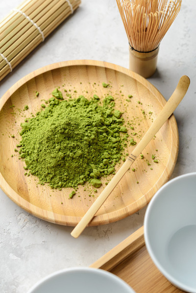 抹茶绿茶粉放在一个木制的圆盘子上，抹茶、竹叶和打蛋器