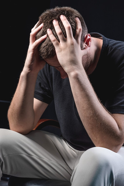 穿着黑色衬衫的年轻英俊男子坐在那里，在黑色背景上抬起他的头。遭受压力时,疼痛