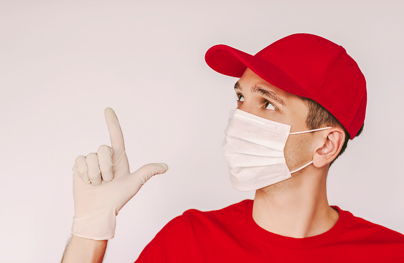 Happy young delivery guy in red uniform, face mask