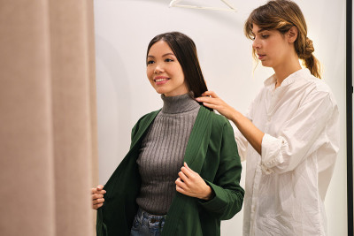 年轻的时尚顾问在现代商店里帮助一个非常积极的亚洲女孩试开襟羊毛衫