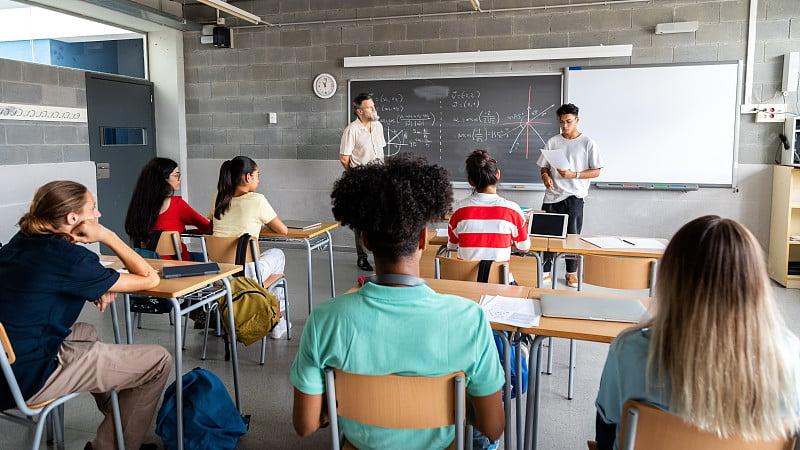 十几岁的亚洲男孩高中学生在课堂上向他的多种族同学和男老师作报告。水平横幅图像。