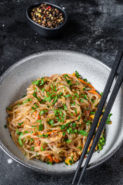 锅热的亚洲玻璃纸面条与鸡肉。黑色背景。俯视图