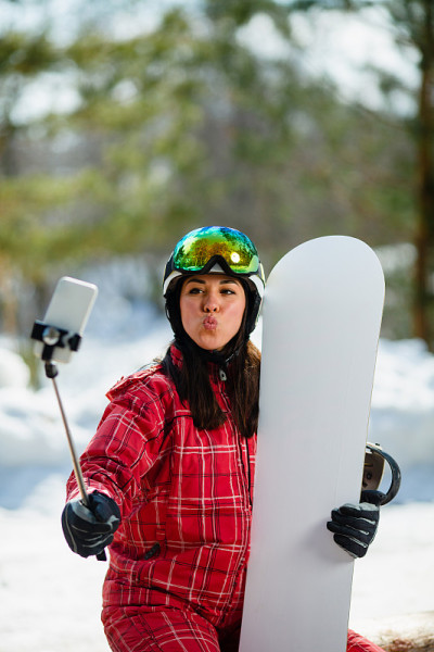 一名女子拿着滑雪板，把智能手机放在棍子上自拍