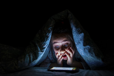小女孩在黑暗中看到床上的手机屏幕很惊讶
