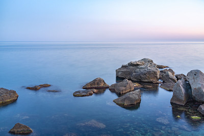 暮色笼罩着荒凉的岩石海滩、海岸线和大海。大海和岩石在夜间的广角视野。