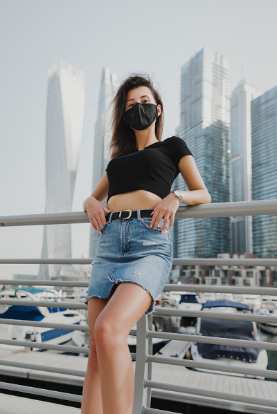 年轻女子身穿黑色t恤和牛仔裙，戴着防护面罩，站在市中心