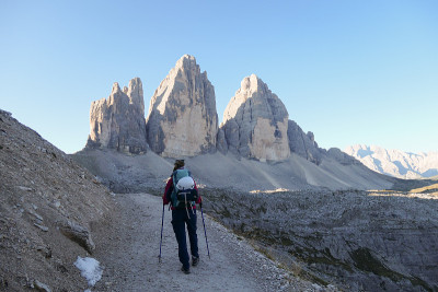 一名身穿粉色夹克的女子在砾石路上徒步旅行，欣赏意大利Dolomites地区的Drei Zinnen山